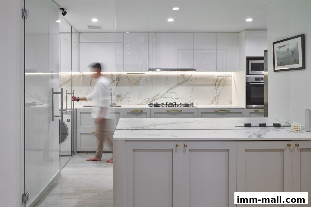 A person walks through a modern, sleek kitchen with marble countertops and grey cabinetry.