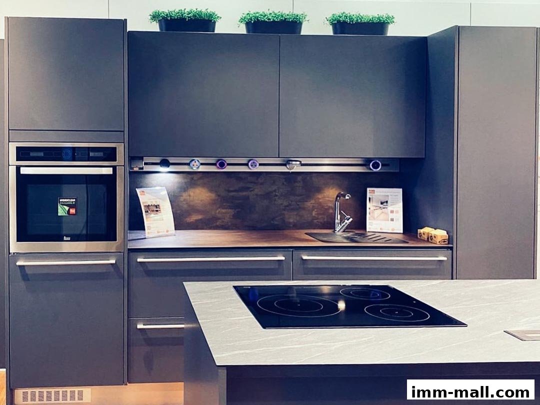 A modern kitchen display featuring dark grey cabinets, an oven, sink, and induction hob.