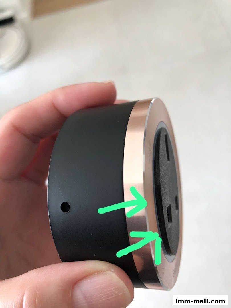 A hand holds a black and rose gold electrical outlet with green arrows pointing to the edge.