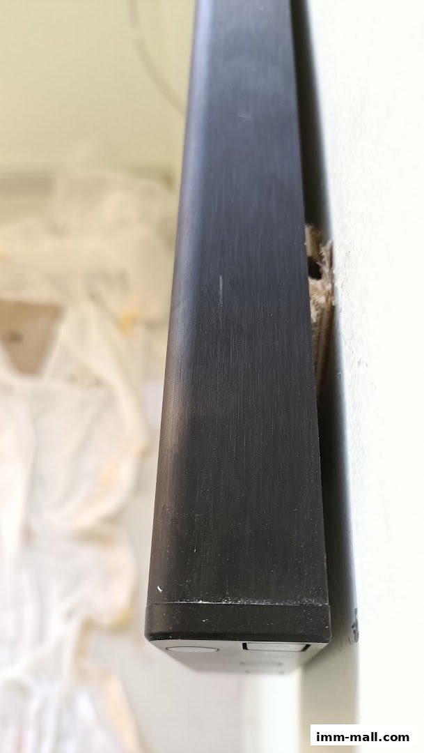 Close-up of a black metal extrusion mounted on a white wall.