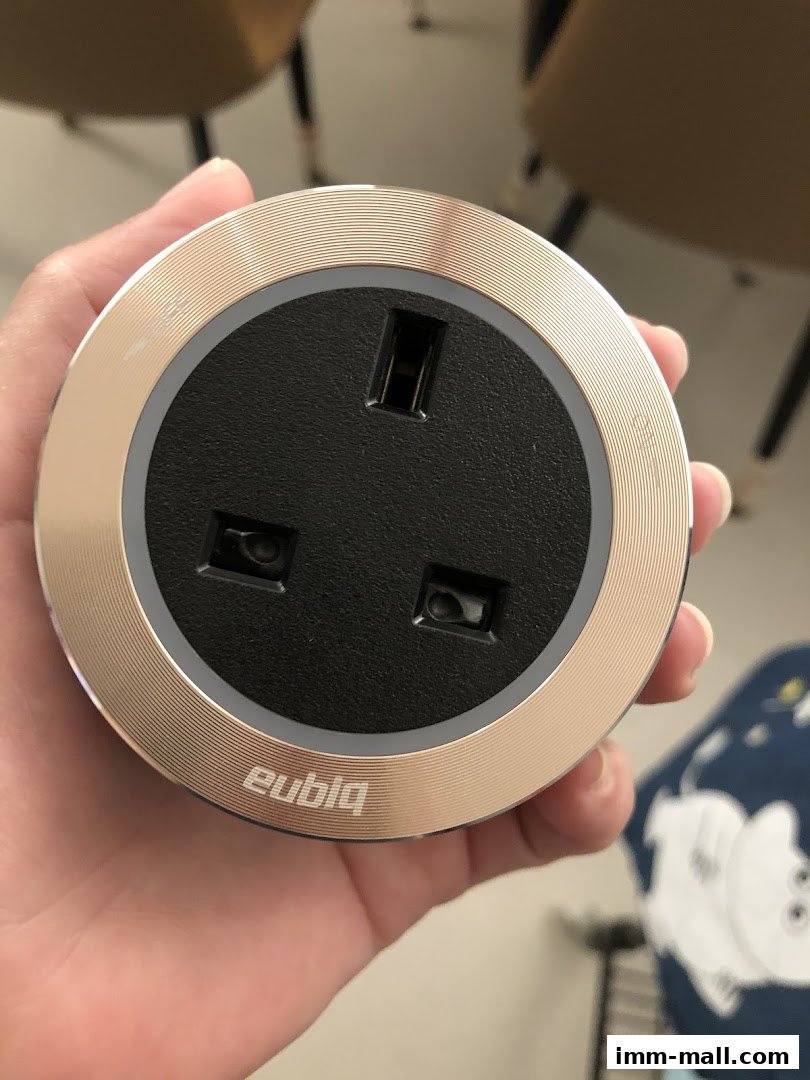 A hand holds a circular Eubiq power outlet with USB ports.
