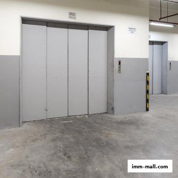 Two large grey elevator doors in a concrete-floored area with yellow and black striped bollards.
