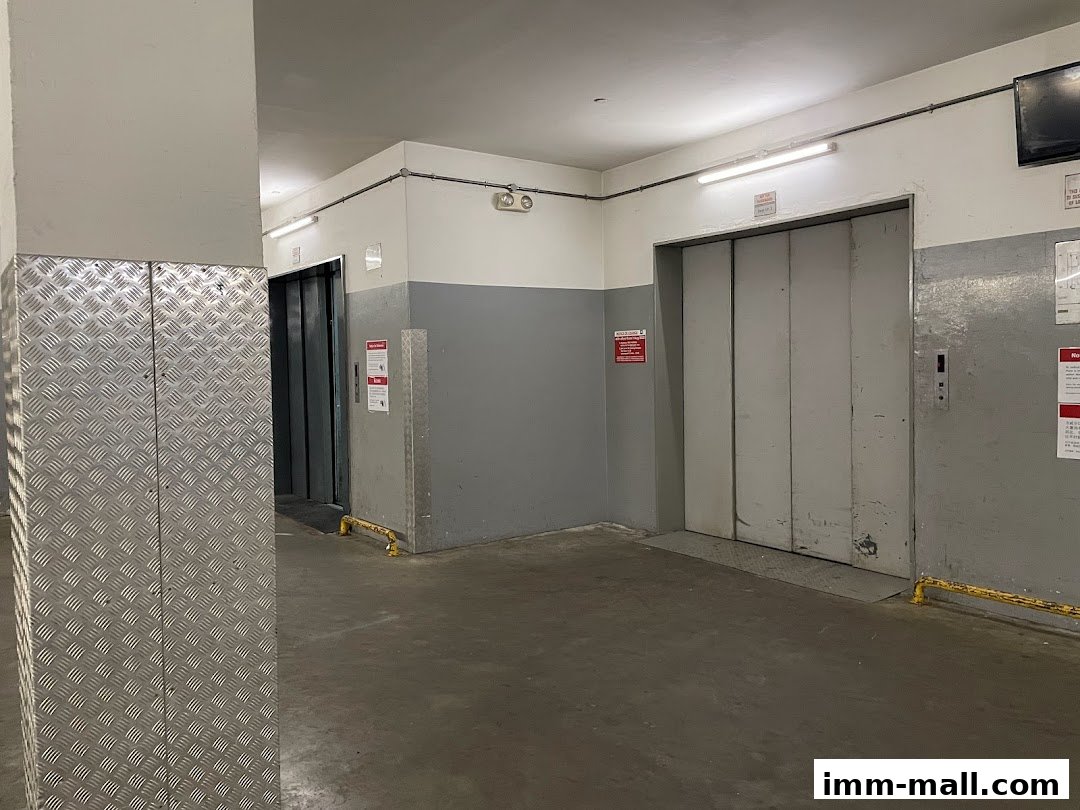 Two elevators are visible in a concrete hallway with metal siding on the left.