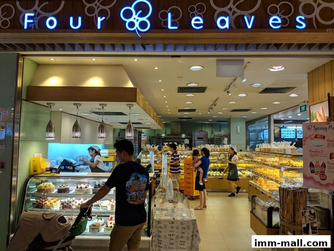 The entrance of a bakery with a display of cakes and bread, and customers inside.