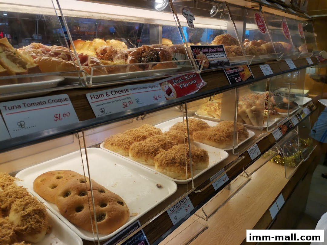 A display case filled with various baked goods, including buns and pastries, at a bakery.