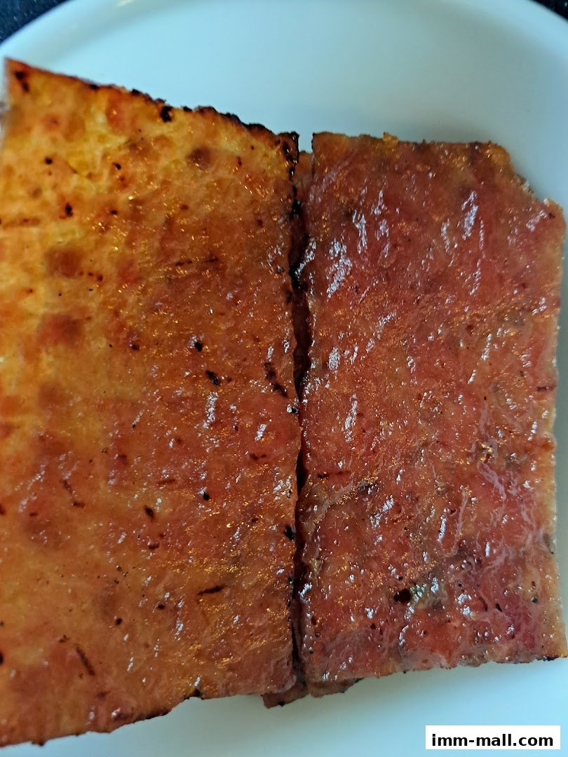 Close-up of two slices of glistening, grilled bak kwa (dried meat) on a white plate.