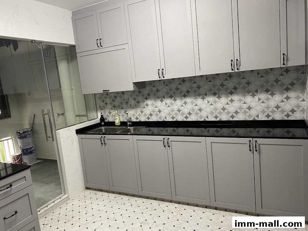 A modern kitchen with grey cabinets, black countertops, and a patterned backsplash.