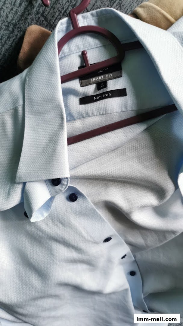 A light blue dress shirt with dark buttons hangs on a hanger.