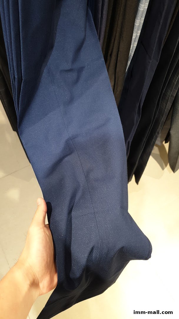 A hand holds a pair of dark blue textured trousers hanging in a store.