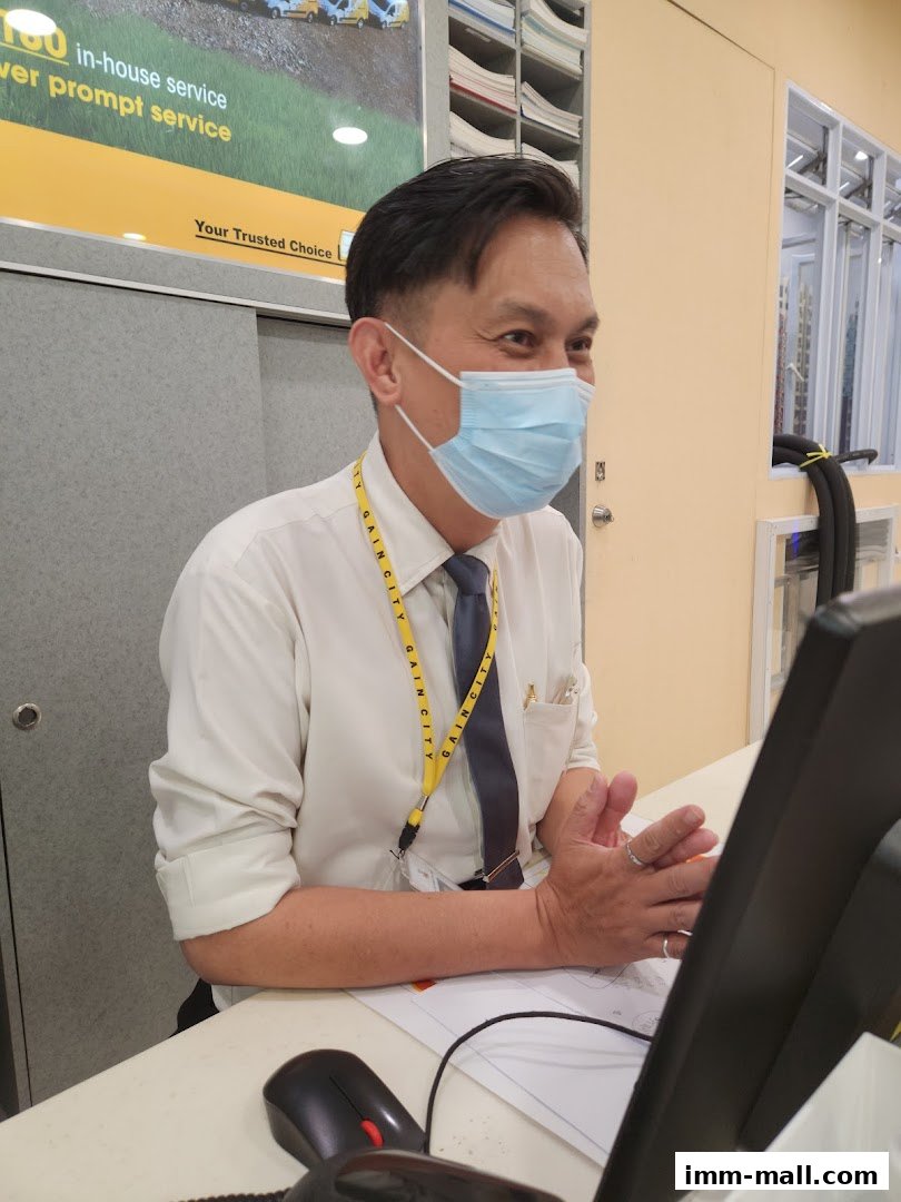 A masked employee at Gain City is shown at a counter with a computer monitor.