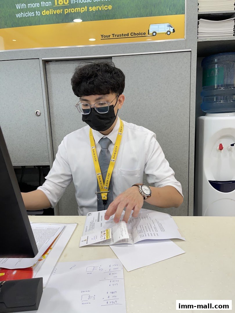 A Gain City employee wearing a mask and glasses assists a customer at a counter.