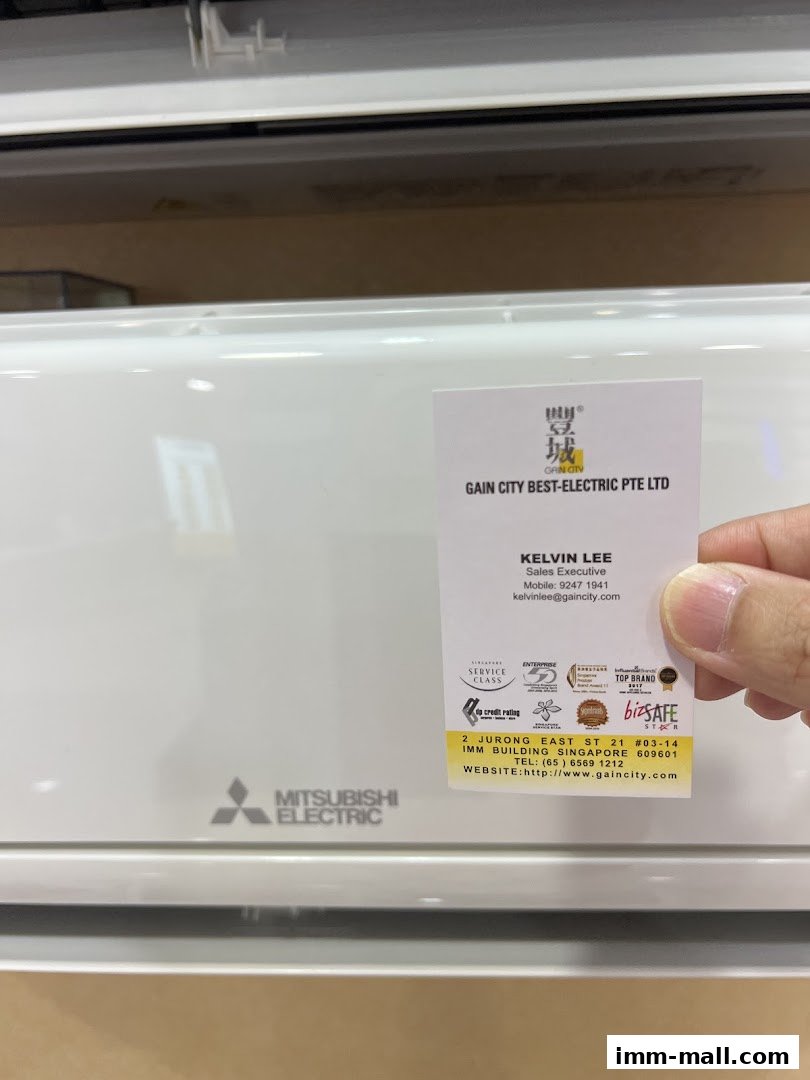 A business card for Gain City Best-Electric Pte Ltd is held in front of a Mitsubishi Electric air conditioner.