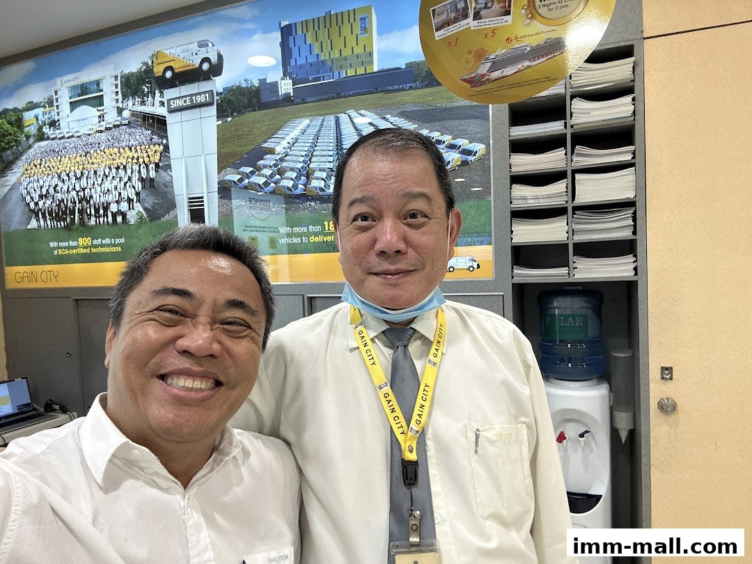 Two smiling men in front of a wall display for Gain City, showcasing their services and staff.
