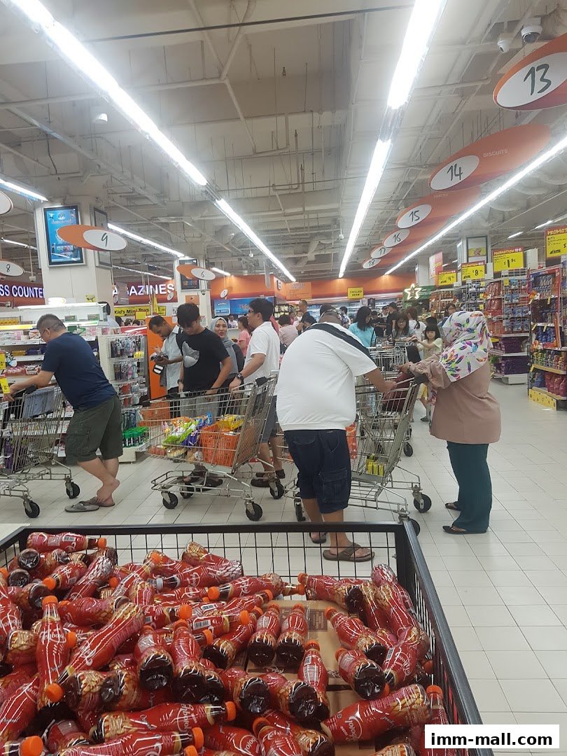 Customers with shopping carts in a supermarket aisle with many bottles of drinks in the foreground.