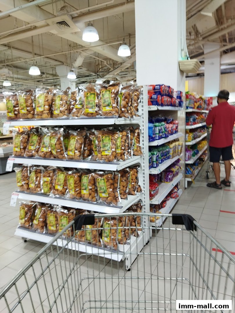 A shopping cart in front of shelves stocked with bagged snacks and other grocery items.