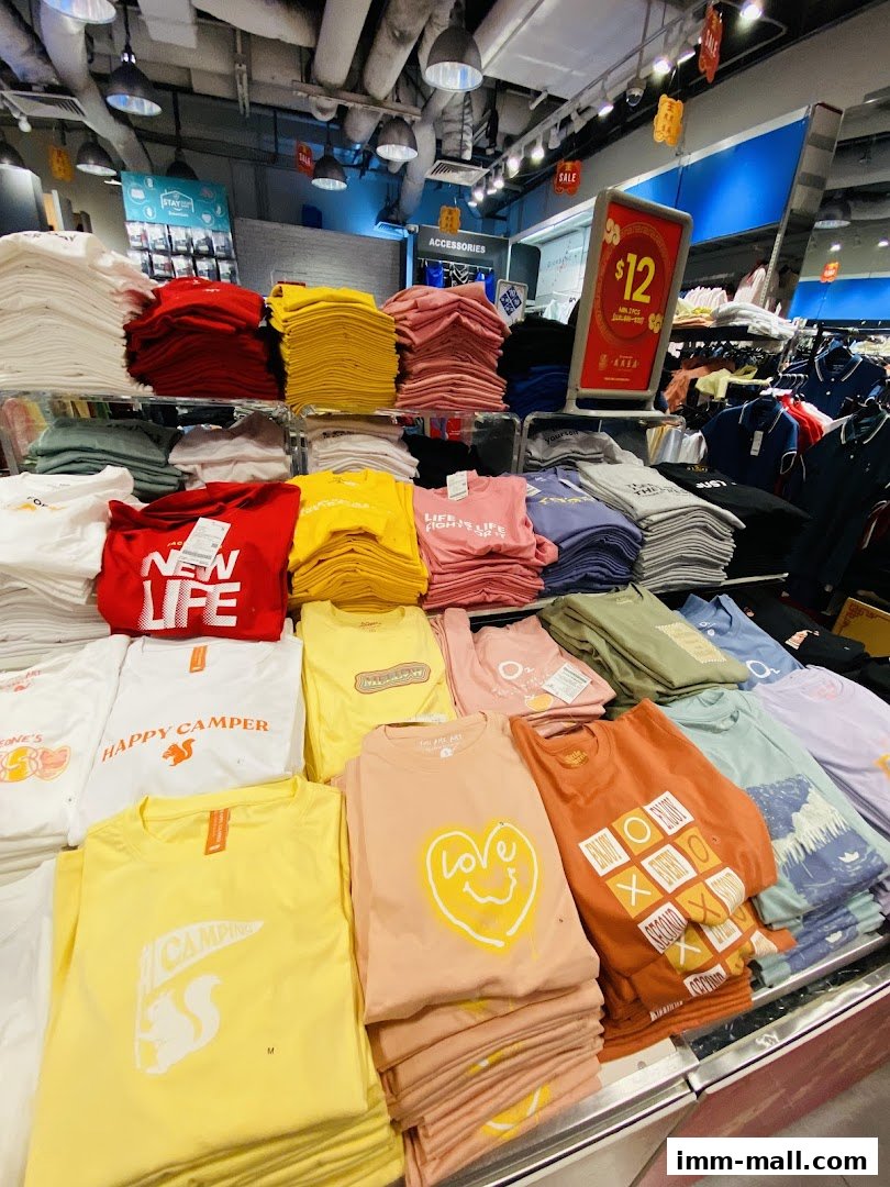 A display of colorful t-shirts with various graphic prints and slogans inside a Giordano Outlet store.