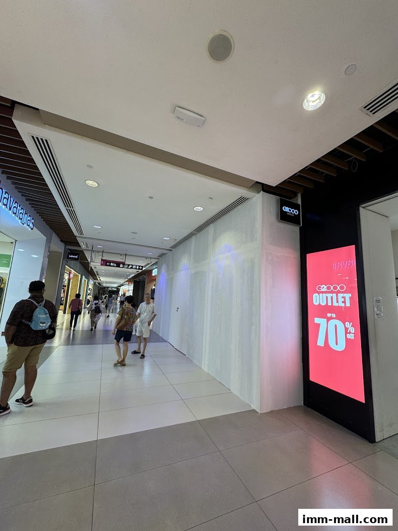 A shopping mall corridor with people walking past a Giordano Outlet store with a large sale advertisement.