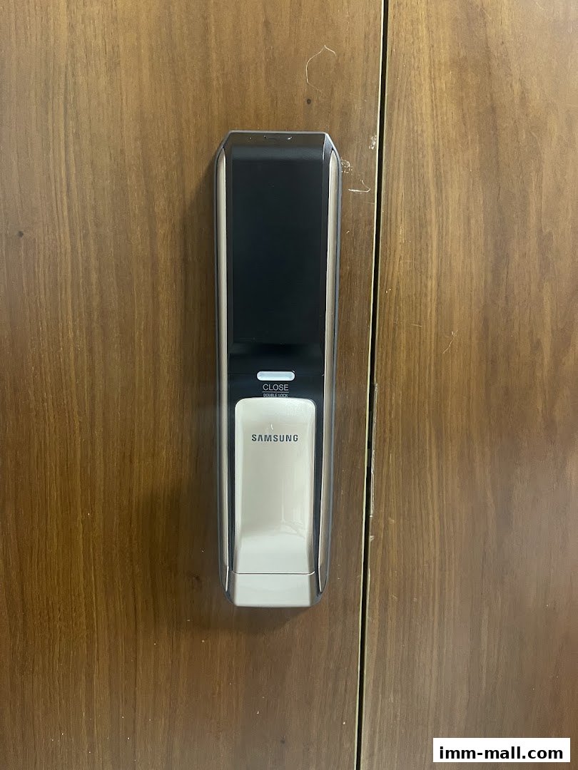 A close-up of a Samsung digital door lock installed on a wooden door.