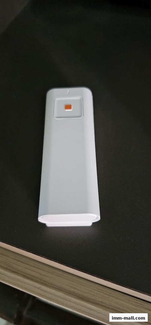 A white electronic device with an orange button on a dark surface.
