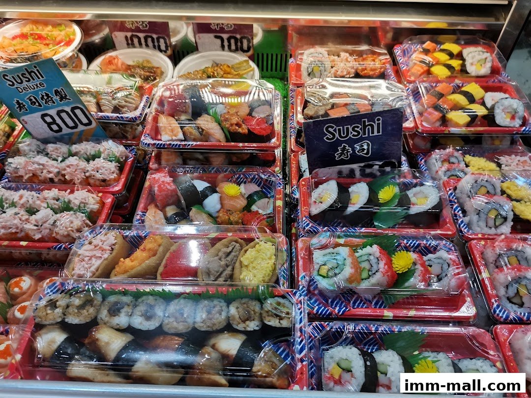 A display of various pre-packaged sushi rolls and other Japanese dishes in plastic containers.