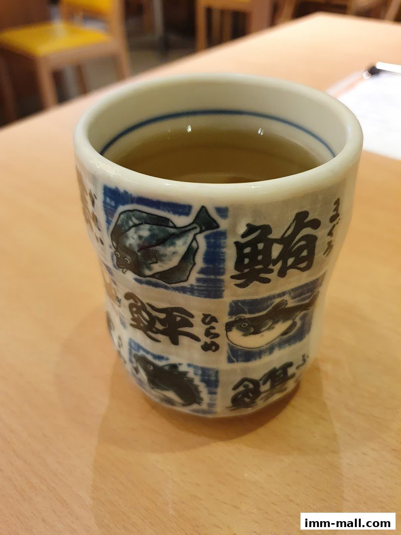 A close-up of a ceramic cup with Japanese fish designs and text, filled with tea.