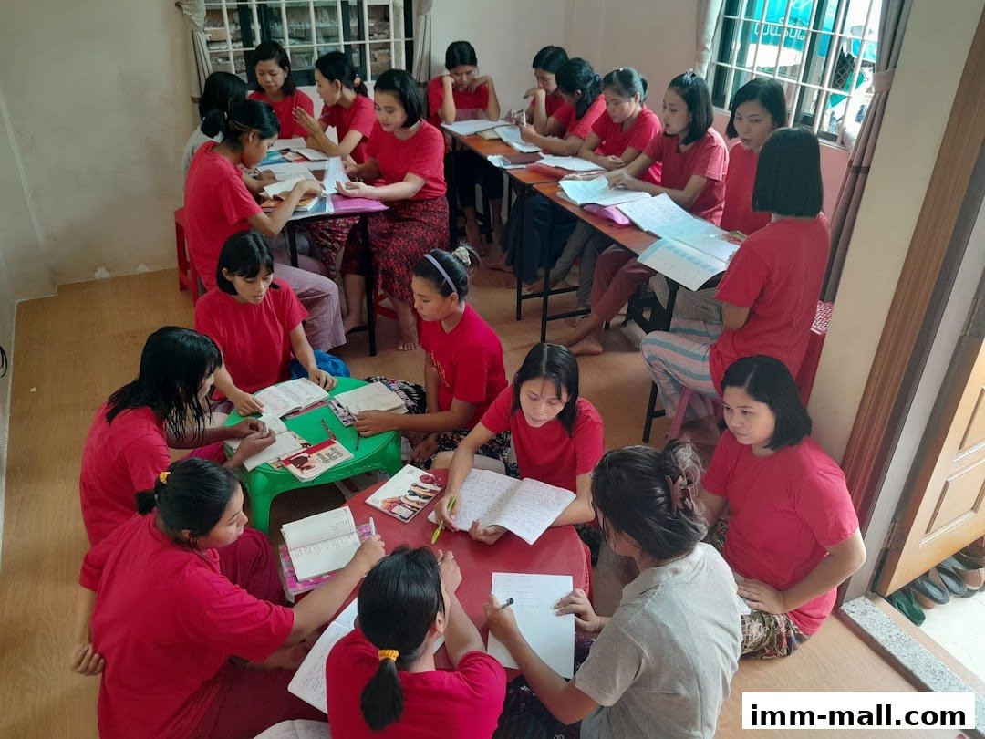 A group of women in red shirts are studying and writing in a classroom setting.