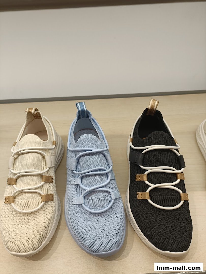 Three pairs of Hush Puppies sneakers in cream, light blue, and black on a wooden shelf.