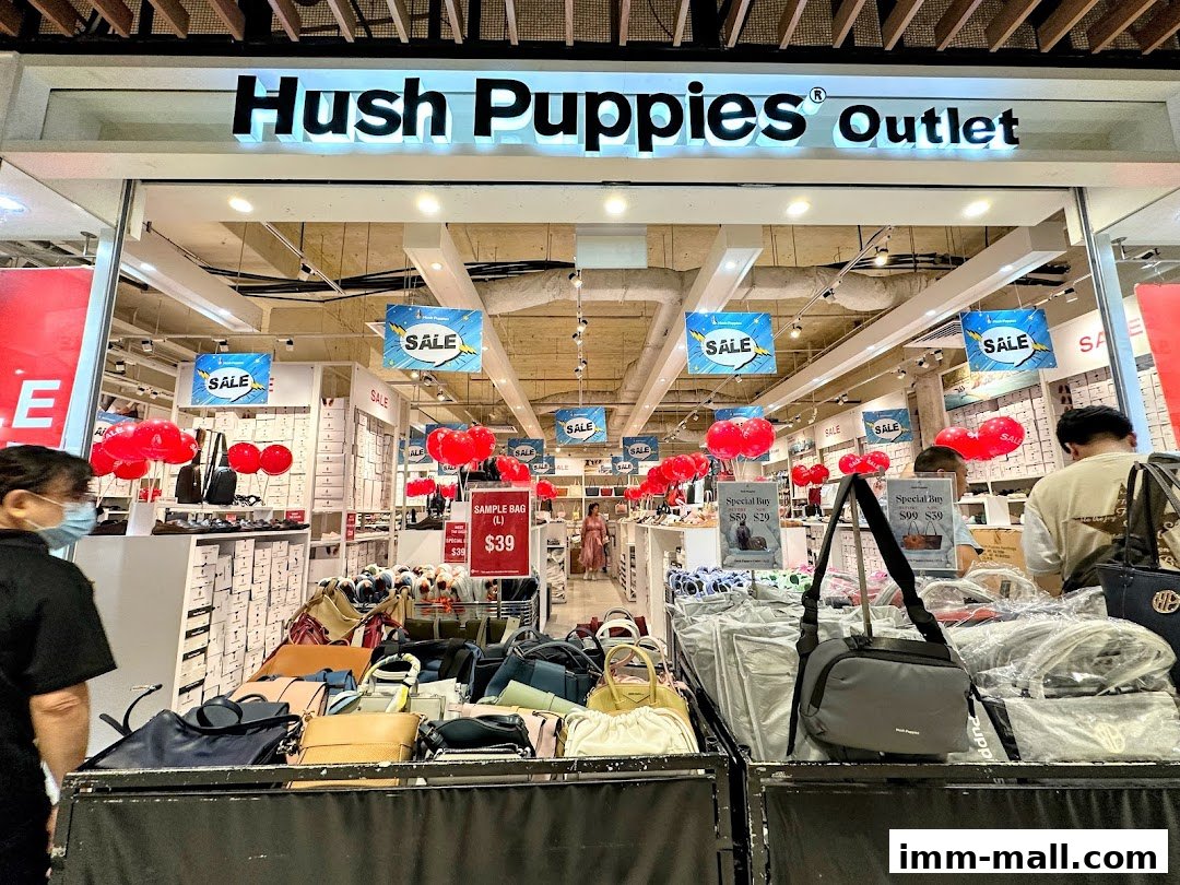 The entrance of a Hush Puppies Outlet store displaying footwear and bags with sale signs.