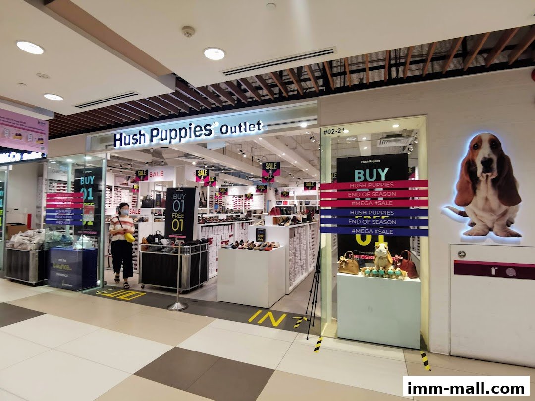 The exterior of a Hush Puppies outlet store with shoes and bags displayed, featuring sale signs.