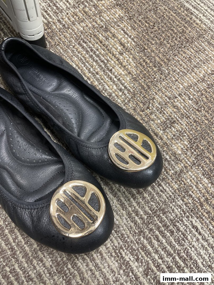 Close-up of black Hush Puppies ballet flats with gold circular embellishments on a textured carpet.