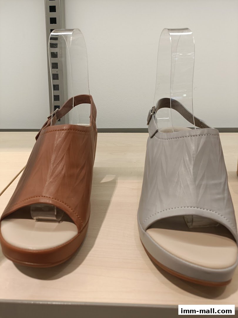 Two stylish Hush Puppies sandals, one brown and one grey, displayed on a shelf.