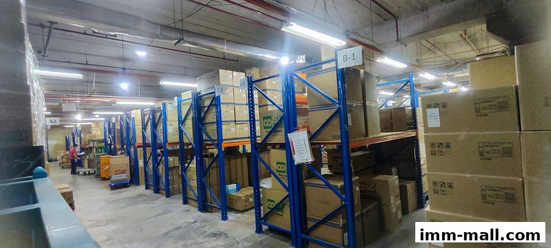 A warehouse interior with tall shelves stacked with boxes, and a person working in the background.