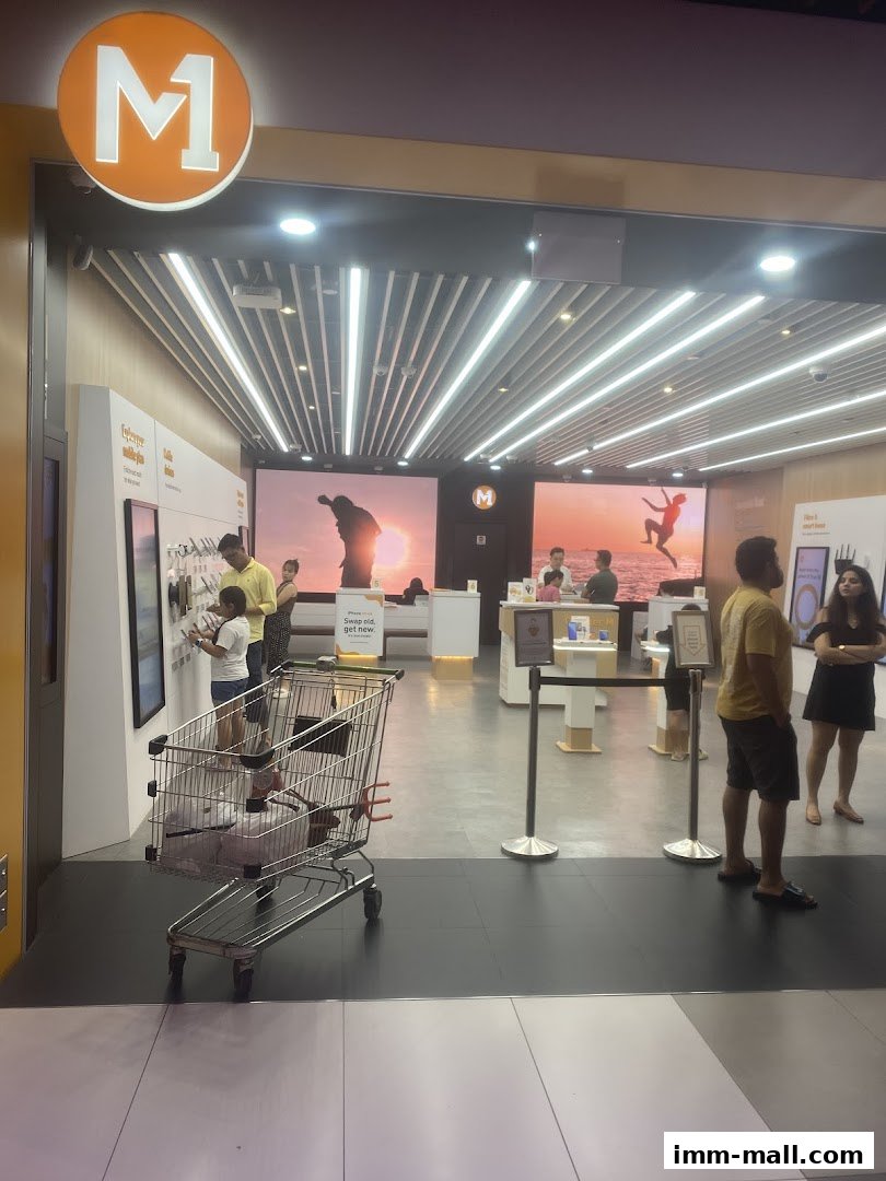 The entrance of an M1 phone shop with customers browsing and a shopping cart.