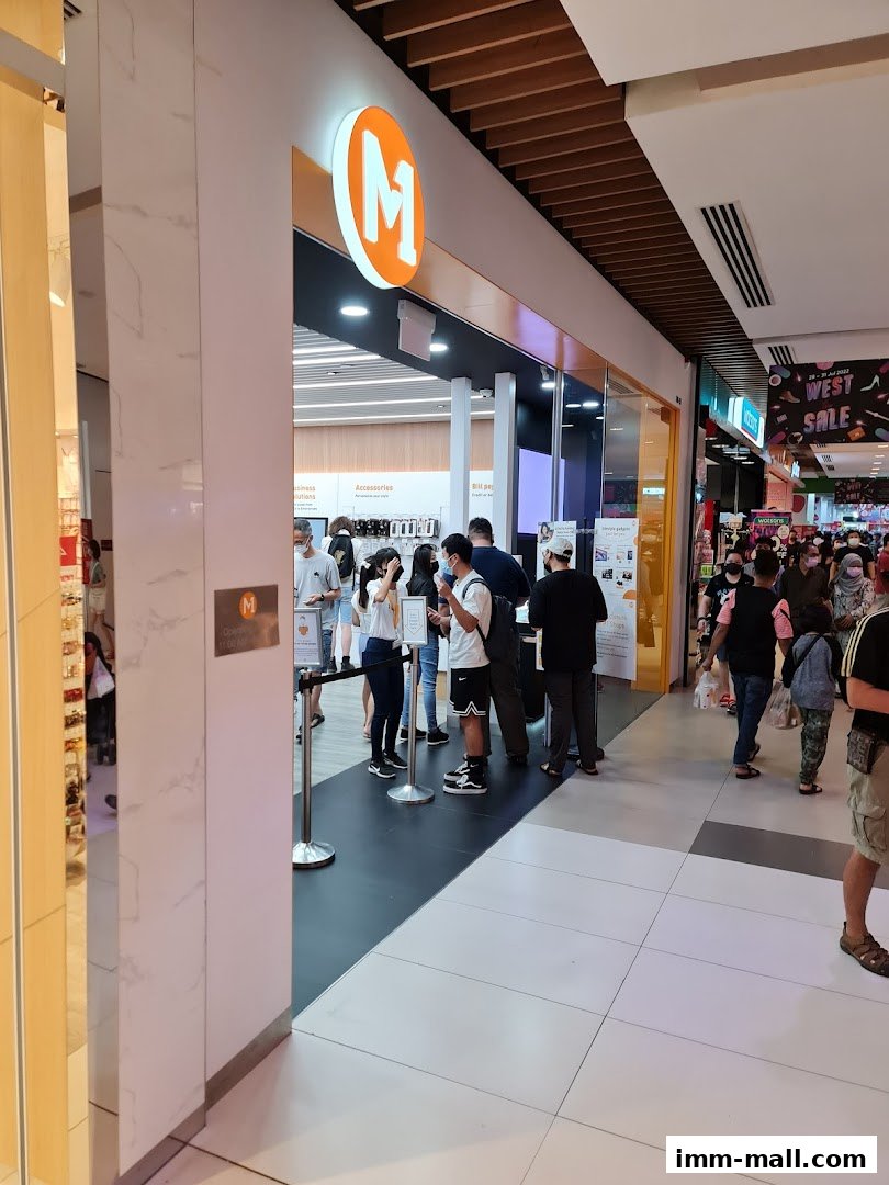 People queuing outside a brightly lit M1 phone shop and internet service provider store.