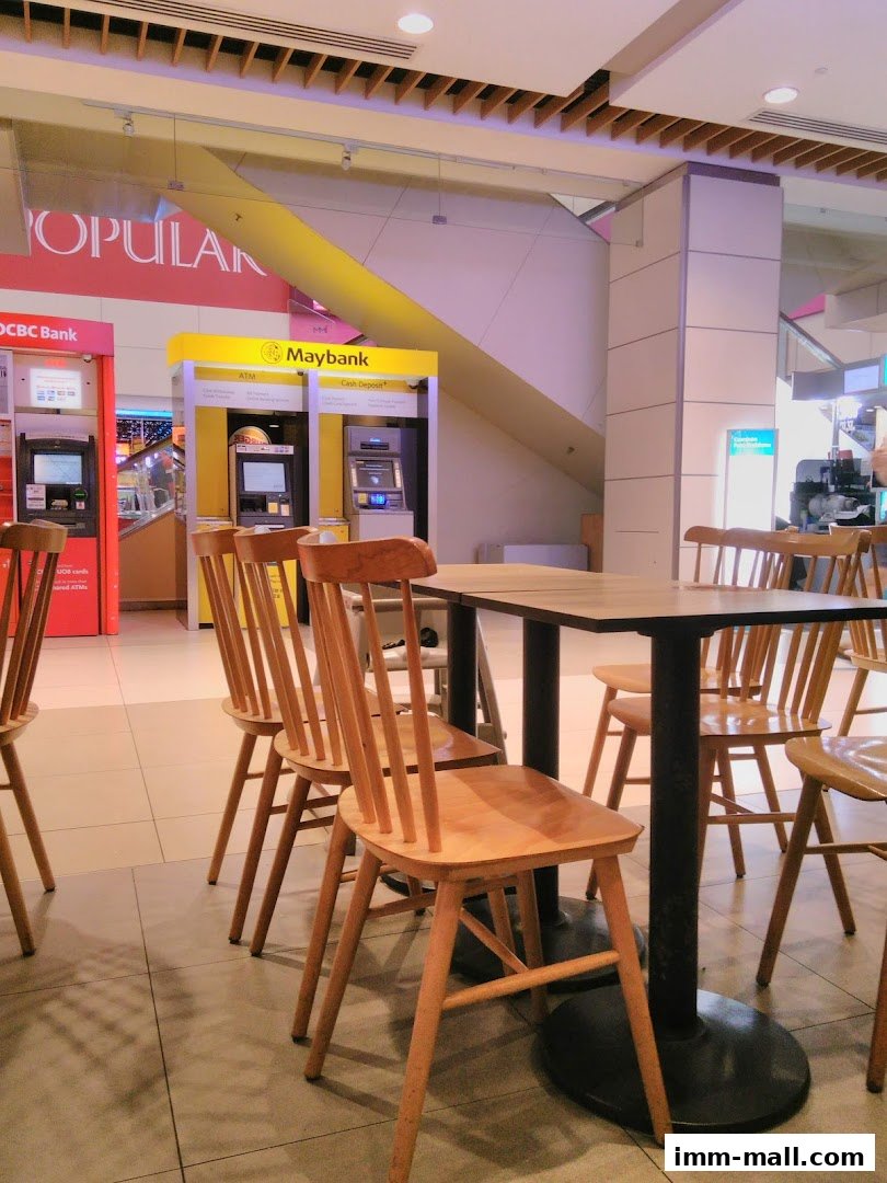 A seating area with wooden chairs and tables in front of Maybank ATMs.