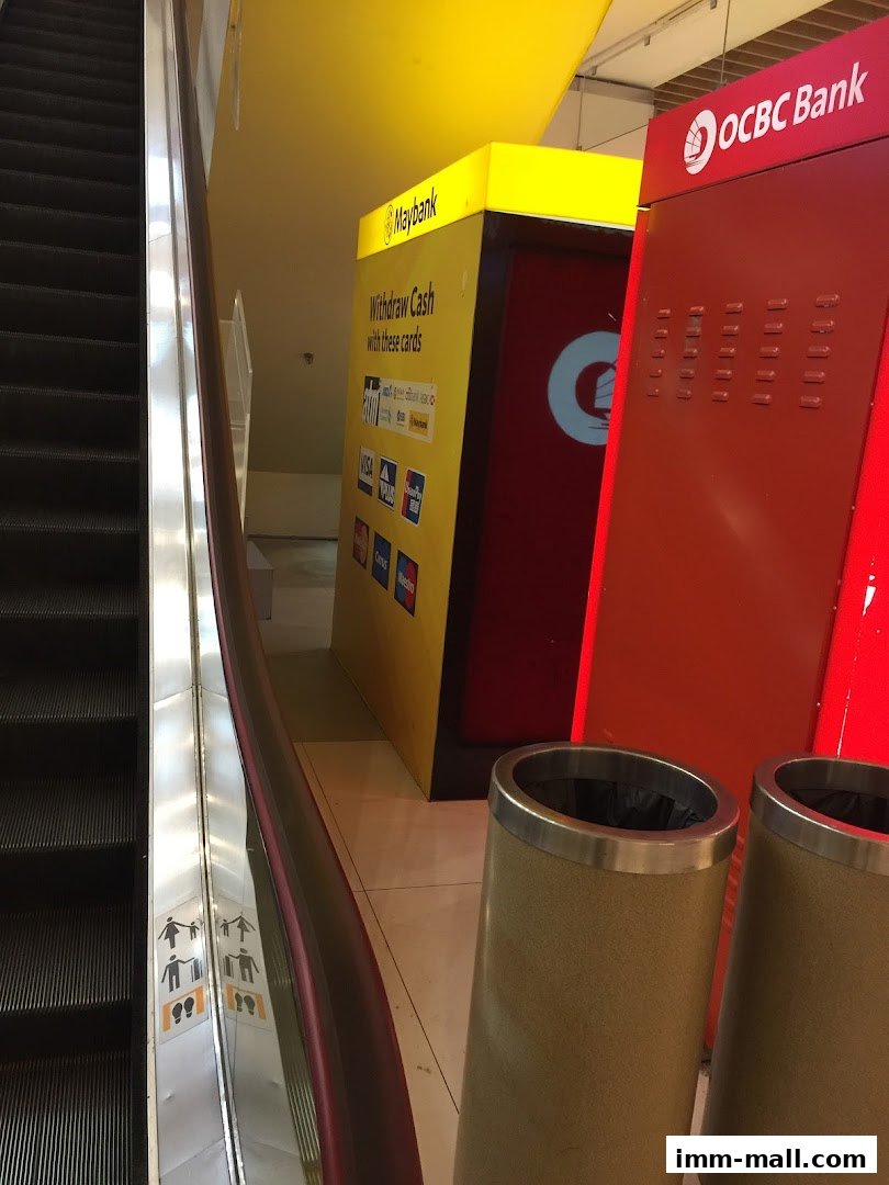 Maybank and OCBC Bank ATMs are located next to an escalator in a shopping mall.