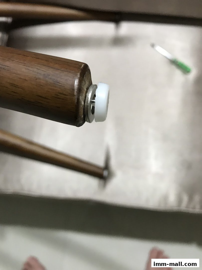 Close-up of a wooden furniture leg with a protective white cap and metal hardware.