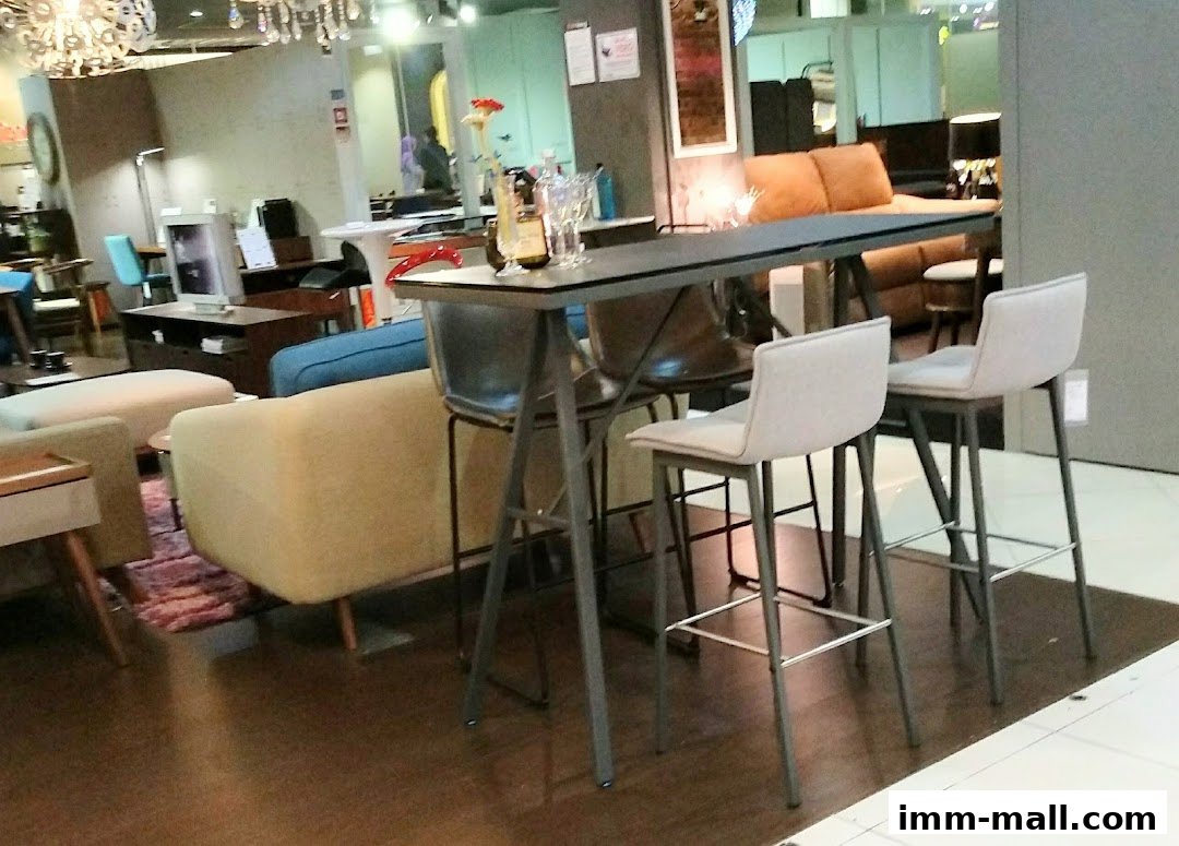 A modern high table with bar stools and sofas in a well-lit furniture store.