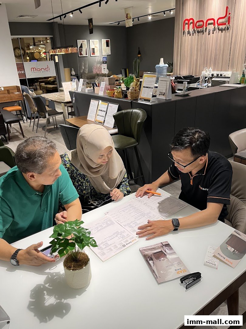 A sales associate discusses a document with customers at a table in a furniture showroom.