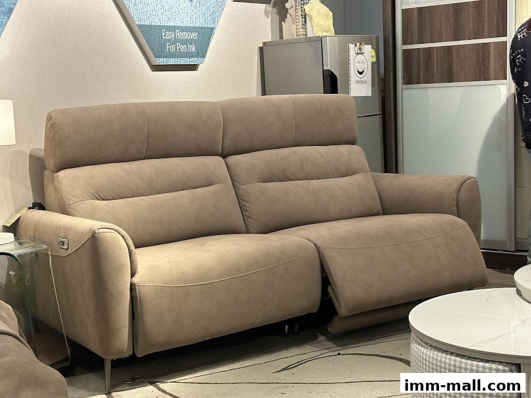A plush, taupe reclining sofa with adjustable headrests and armrests in a furniture showroom.