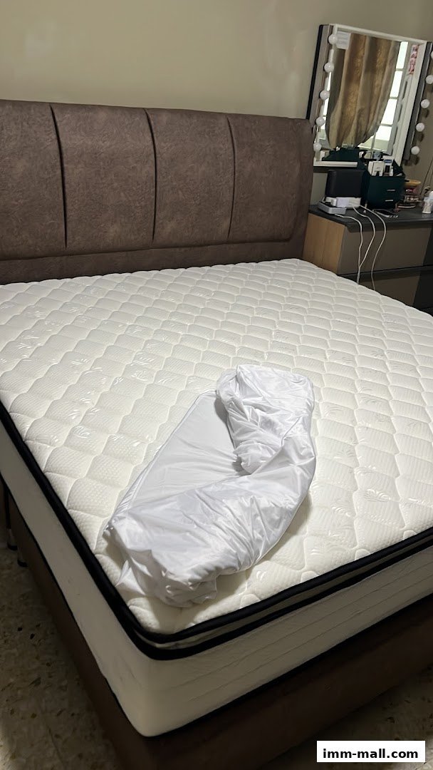 A plush mattress with a brown upholstered headboard and white bedding.