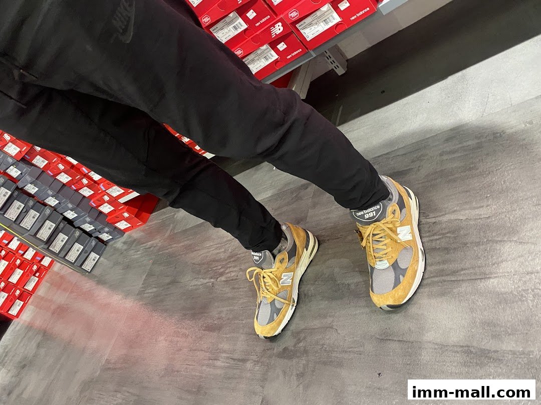 A person wearing New Balance 991 sneakers stands in a store with shelves of shoe boxes.