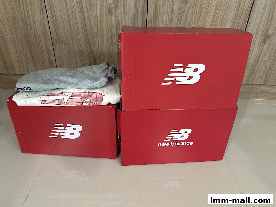 New Balance branded red boxes with clothing items inside, stacked on a tiled floor.