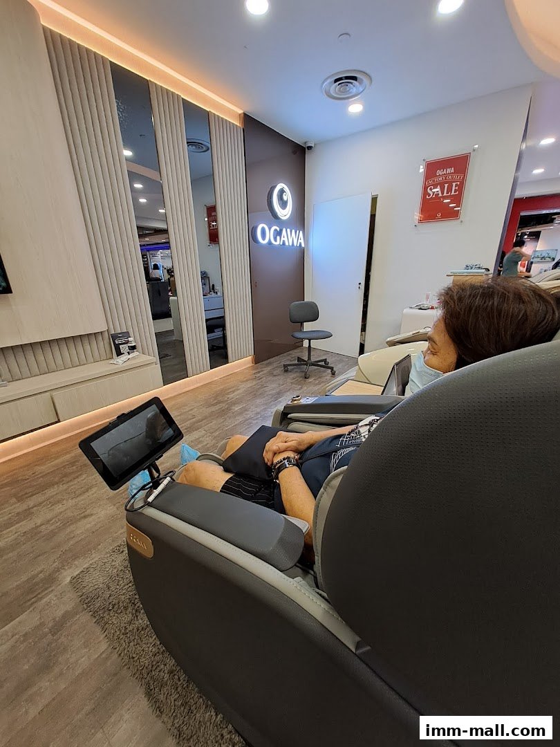 A person relaxing in an OGAWA massage chair inside a modern retail store.