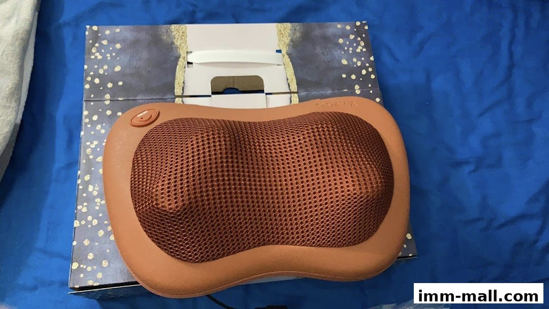 A brown massage pillow with a mesh surface sits on its packaging.
