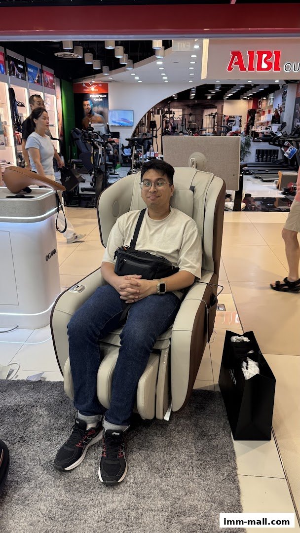 A man sits in a massage chair in a retail store, with other fitness equipment visible.