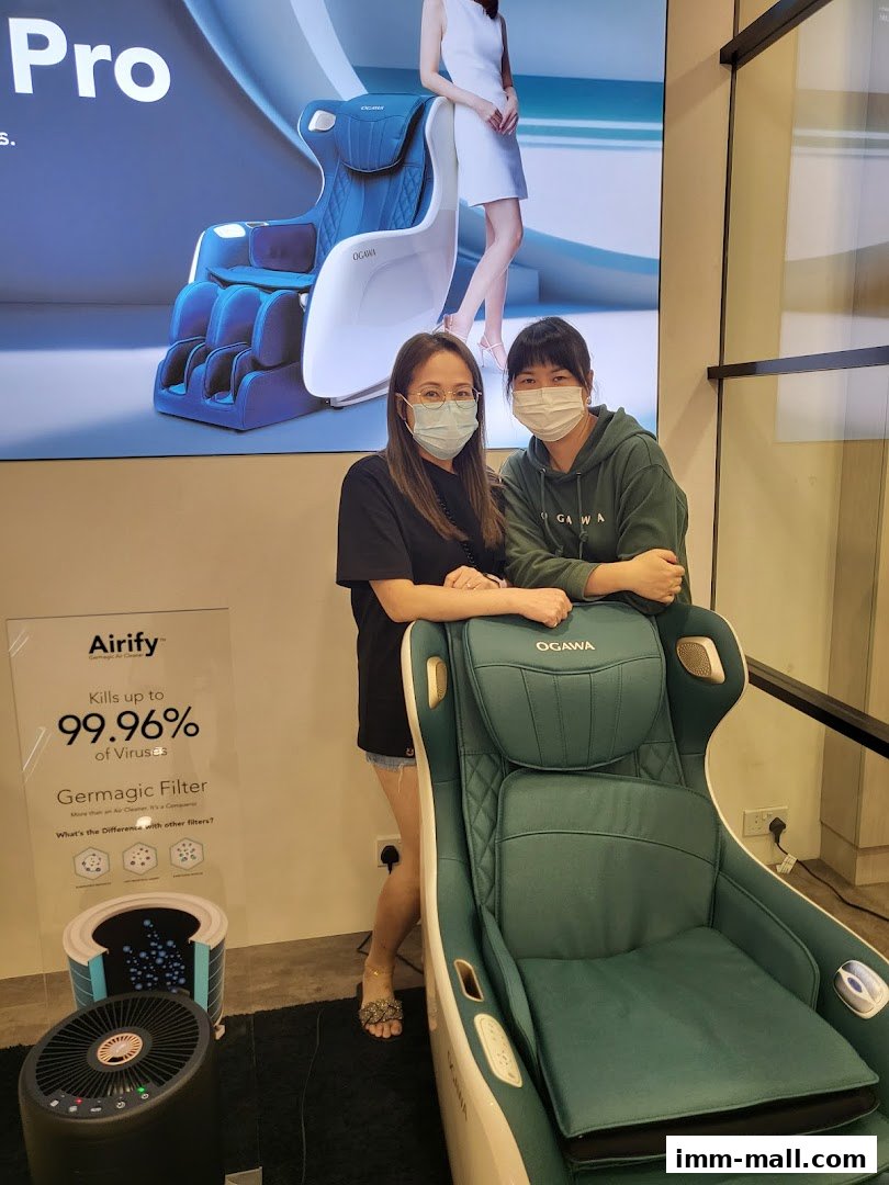 Two women stand next to an OGAWA massage chair and an Airify air purifier.