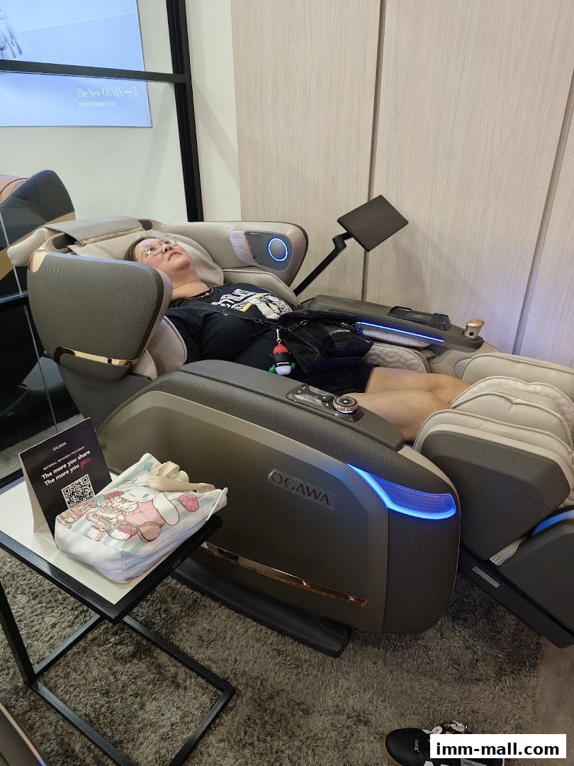 A person relaxes in an OGAWA massage chair, with promotional materials nearby.
