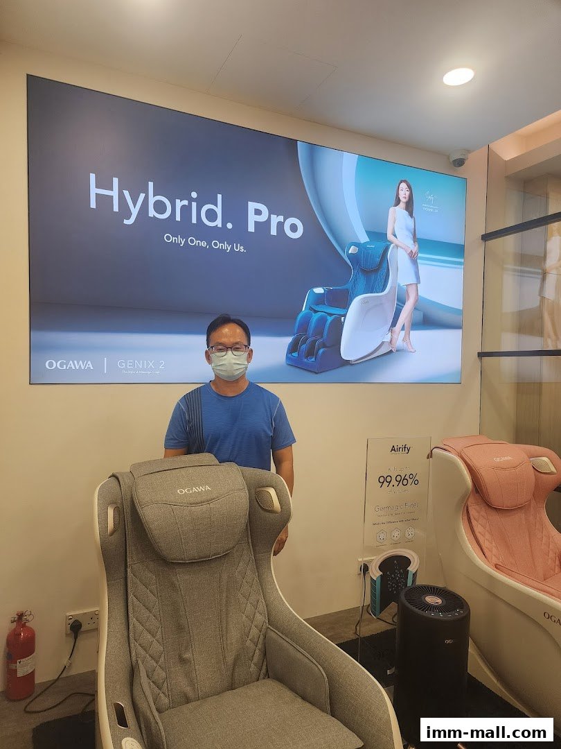 A man stands in front of an OGAWA massage chair display featuring the Hybrid. Pro.