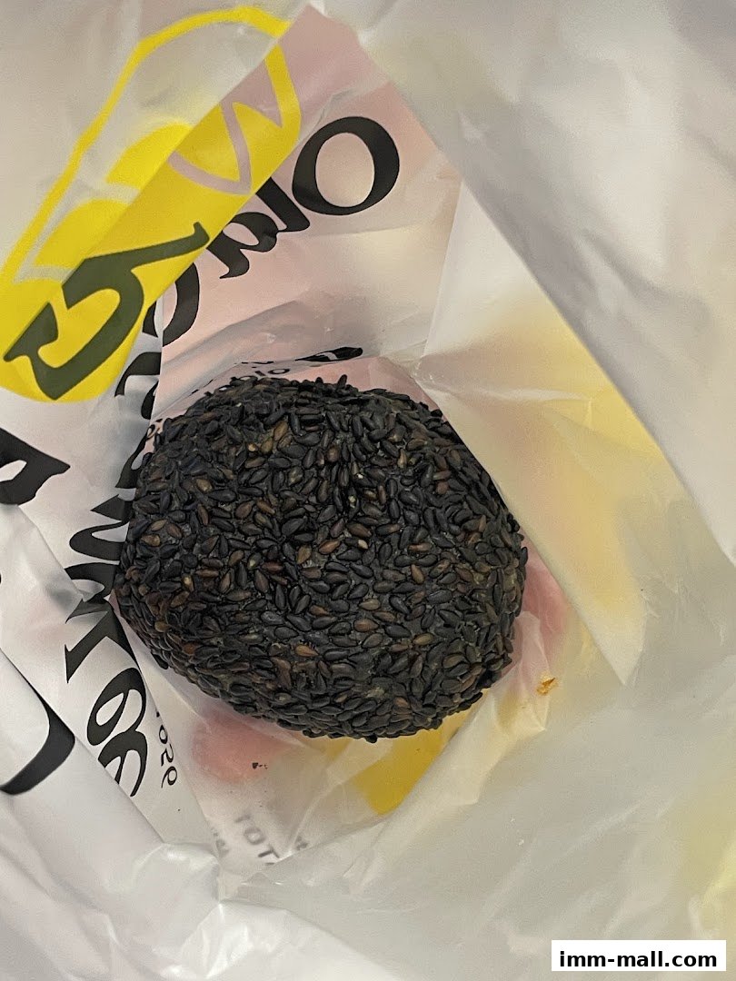 A black sesame coated pastry sits inside a white paper bag with yellow and pink branding.